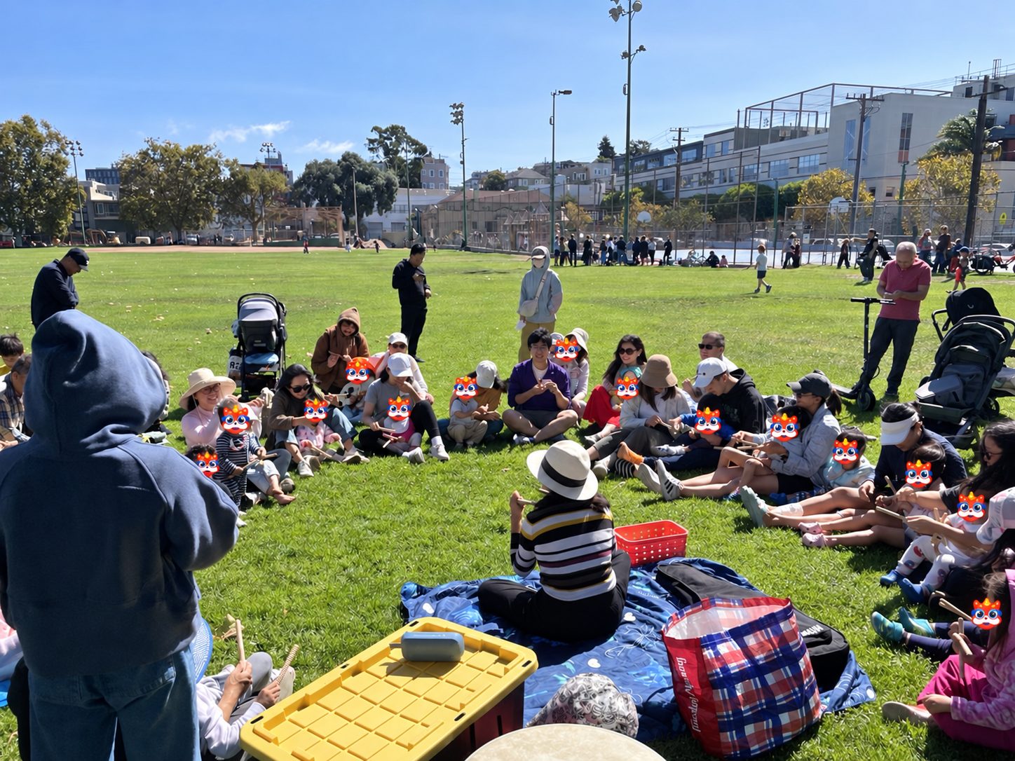 Families sitting in a big circle on the grass, kids playing rhythm sticks